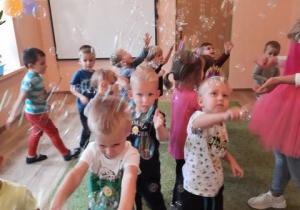 Grupa dzieci bawi się bańkami mydlanymi, próbując je złapać.